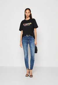 Black cotton t-shirt featuring a multicolored "Guess love club" graphic. Paired with light blue slim-fit jeans and black strappy heels.