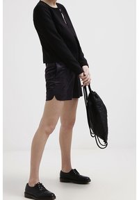 Haut noir à manches longues, short violet avec un ourlet festonné, chaussures noires à lacets et sac à dos noir texturé. Design minimaliste.
