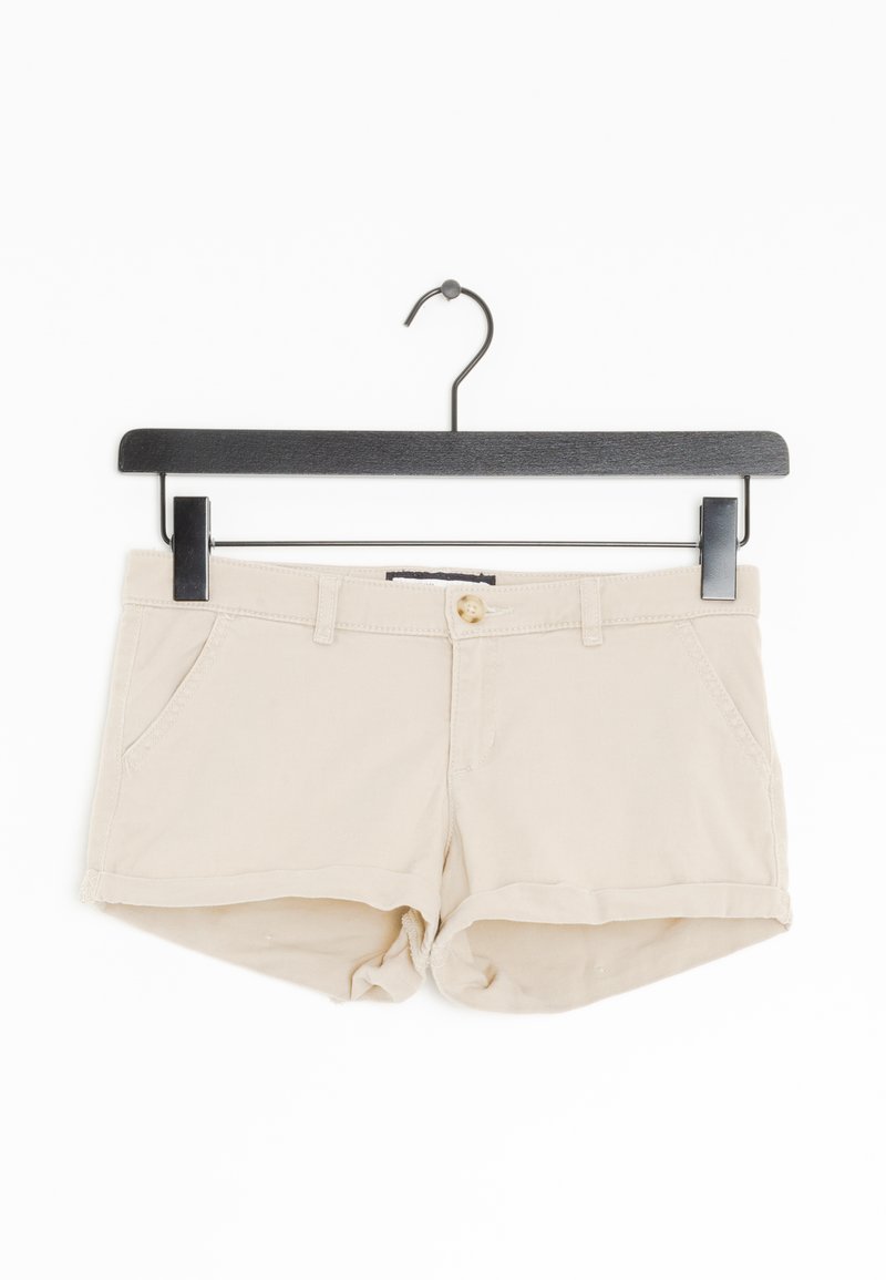 Shorts in cotone beige con chiusura a zip e bottone, due tasche frontali, orli arrotolati e una clip sospesa. Texture liscia e design semplice.
