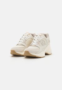 Baskets de sport beiges présentant un mélange de textures lisses et en daim, avec une semelle épaisse et des lacets blancs ; logo embossé sur le côté.