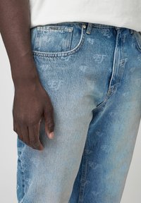 Ljus tvättade denimjeans med subtila logomönster, femfickdesign och en klassisk passform, med knappstängning och bältesömmar.