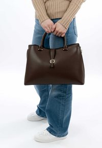 Borsa a mano in pelle marrone con un design strutturato, caratterizzata da un accento centrale in metallo circolare e due manici superiori. Rifinita con una texture liscia.