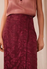 Bordó szoknya finom levélmintával, texturált anyagból készült. Középhosszú kialakítású, oldalsó hasítékkal a részletek kiemelésére.