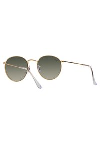 Occhiali da sole rotondi in metallo dorato con lenti grigie sfumate. Caratteristiche includono astine sottili e puntali trasparenti. Design minimalista, montatura leggera.