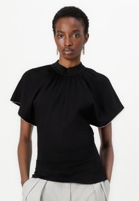 Black top with a high neckline, short flutter sleeves, and gathered detailing. Made from stretch fabric, designed for a fitted silhouette.