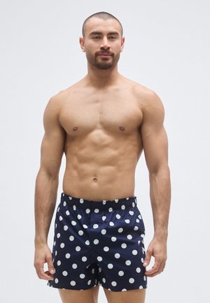 Férfi tengerészkék fürdőnadrág fehér pöttyökkel, rugalmas derékpánttal és laza szabással. Az anyag könnyűnek és simának tűnik.