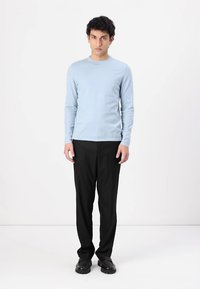 Himmelblaues Langarmhemd kombiniert mit schwarzen Hosen. Das Hemd hat einen runden Ausschnitt und eine taillierte Form; die Hose ist gerade geschnitten und hat keine Textur.