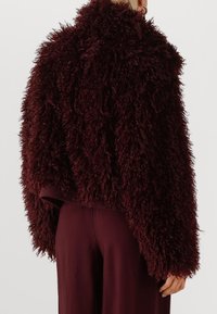Burgundy faux fur jacket with a cropped design, textured shaggy surface, wide sleeves, and contrasting smooth fabric at the hem.