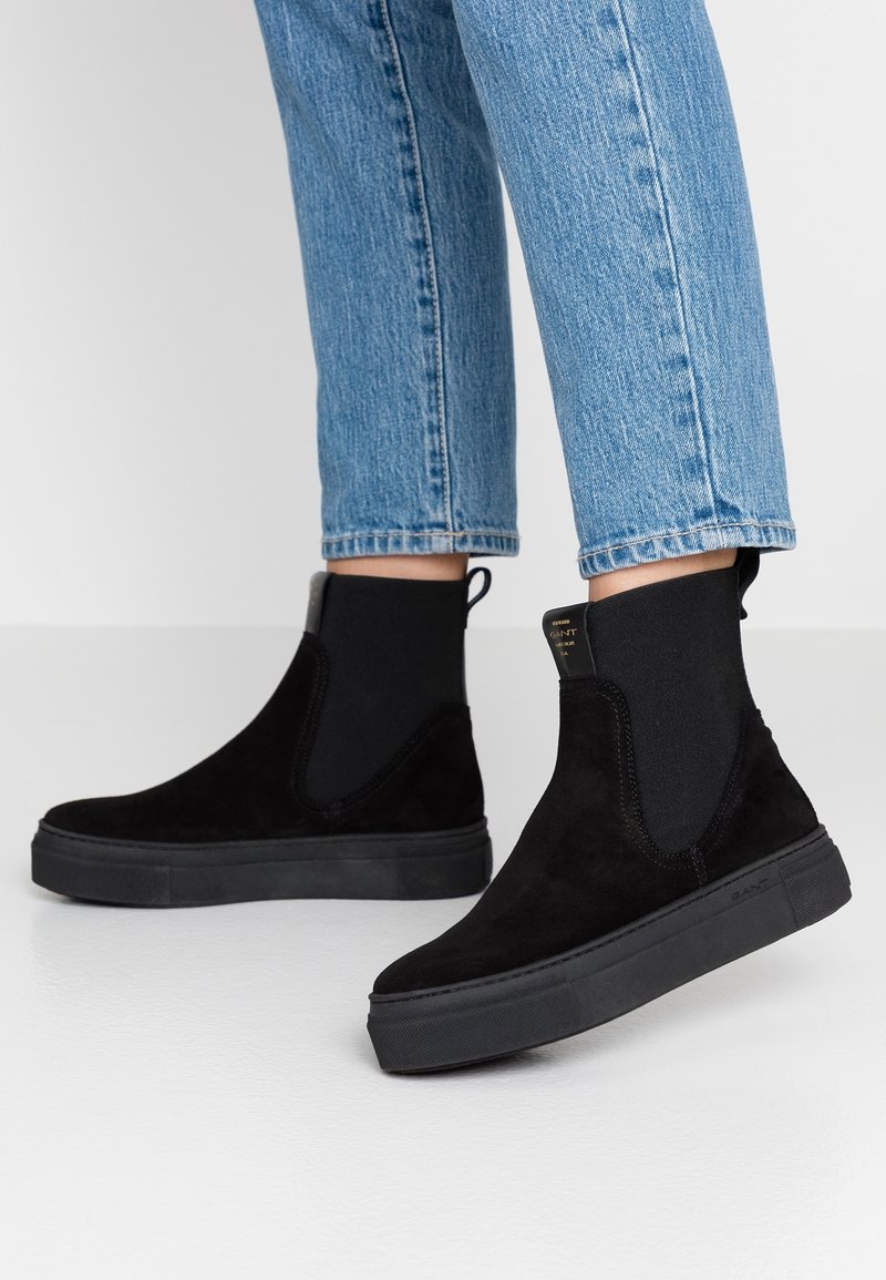 Botas de tobillo de ante negro con paneles laterales elásticos y suelas de goma negra. Presenta un tirador y acentos de costura mínimos.