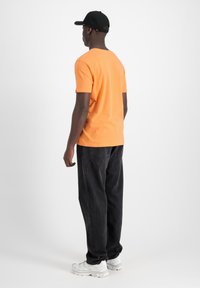 Tricou din bumbac portocalie cu mâneci scurte, asortat cu blugi negri. Ținuta este completată cu pantofi sport albi și o șapcă neagră.