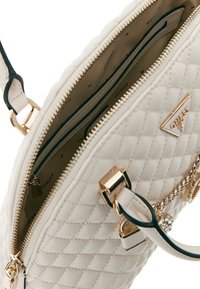 Sac à main matelassé blanc avec quincaillerie dorée, doté d'une fermeture éclair, de plusieurs compartiments intérieurs et d'un accent de chaîne décoratif.
