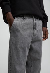 Grå denimbyxor med en lös passform, med synliga sömmar, sidofickor och ett standard midjeband. Tyget har en mjuk textur.