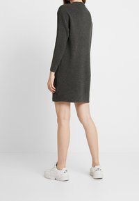 Robe-pull côtelée gris foncé à manches longues, longueur genou, tissu texturé, fentes latérales, portée avec des baskets blanches. Vue de dos.