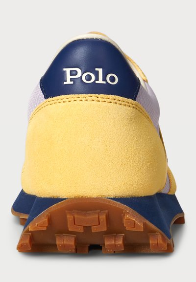 Gul och marinblå sneaker med en mockaklack, meshovandel, gummiyttersula och "Polo"-logotyp på baksidan. Har texturerade detaljer och robust konstruktion.