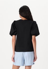 Black puff-sleeve top made of textured fabric, featuring a round neckline, paired with light blue striped shorts.