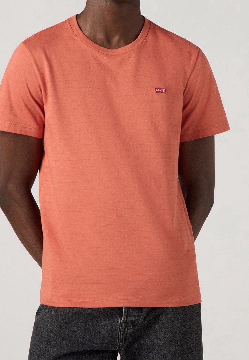 T-shirt corail en coton, avec un col rond, des manches courtes et de subtiles rayures horizontales. Logo rouge Levi's sur la poitrine.