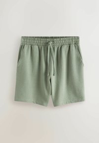 Shorts en tissu texturé vert clair avec taille élastique, cordon de serrage et poches latérales, étalés à plat sur un fond neutre.