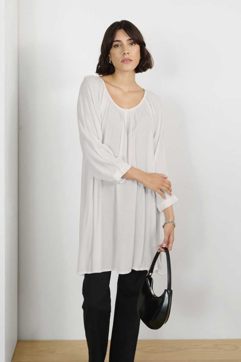 Lange mouwen, lichtgewicht crème tuniek met een ronde halslijn en geplooide details. Gecombineerd met op maat gemaakte zwarte broek en een zwarte handtas.