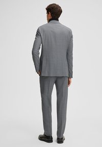 Grau gemustertes Anzug mit Schlitzrevers, schmaler Passform und strukturierten Schultern. Kombiniert mit passenden Hosen und schwarzen, glänzenden Schuhen.