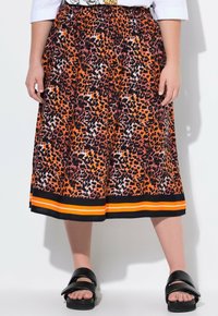 Orange og sort leopardmønster nederdel med elastisk talje, prydet med en sort kant, der er fremhævet af to orange striber. Båret med sorte sandaler.