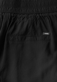 Svarta shorts med elastisk midja, med en liten bakficka och en metalletikett märkt "CECIIL." Slät tygtextur.