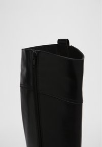 Svarta läderstövlar med dragkedja på sidan, slät yta och en ögla högst upp.