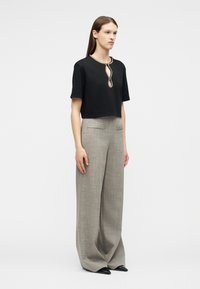 Mujer con una blusa negra de manga corta con cuello decorativo, pantalones grises de pierna ancha y talle alto, y zapatos negros puntiagudos.