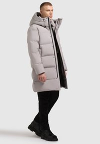 Gai pelēks pūkains mētelis ar augstu apkakli, priekšējo rāvējslēdzēju un lielām kabatām; saderēts ar melniem biksēm un melniem zābakiem. Gluda, mīksta tekstūra.