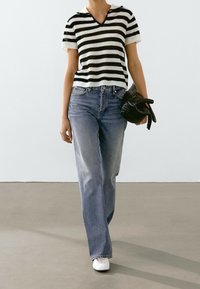 Haut en tricot à rayures noir et blanc à manches courtes, jean large bleu délavé, et baskets blanches, accompagné d'un sac à main noir.