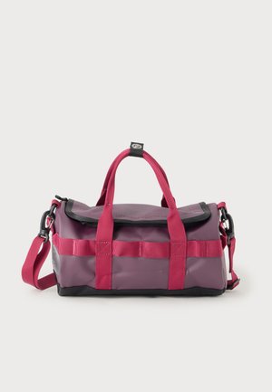 Lille lilla rejsetaske med pink stropper, bærehåndtag og justerbar skulderrem mod hvid baggrund.