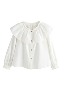 Chemise blanche boutonnée avec un tissu texturé, grand col volanté et manches longues avec poignets élastiques. Dotée de boutons en bois sur le devant.