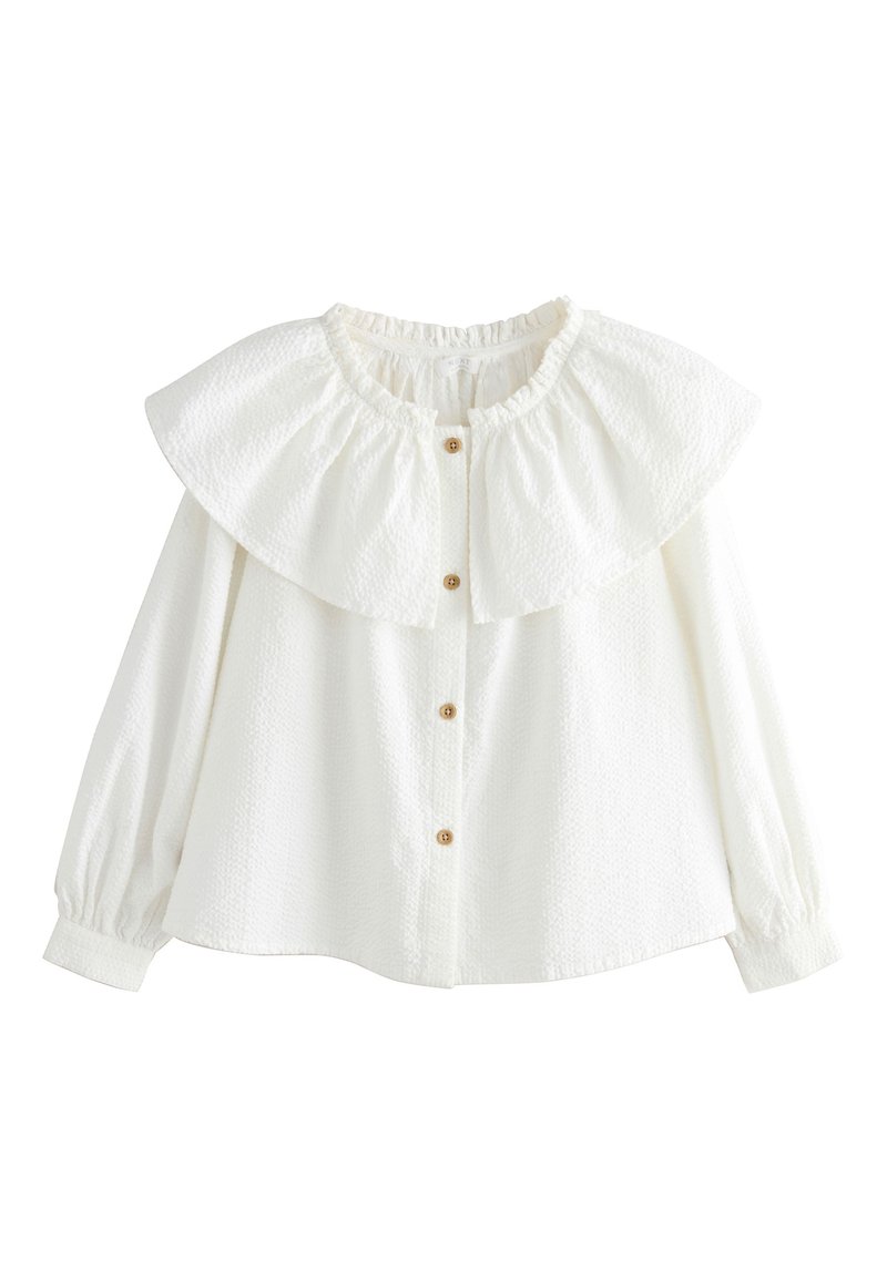 Chemise blanche boutonnée avec un tissu texturé, grand col volanté et manches longues avec poignets élastiques. Dotée de boutons en bois sur le devant.
