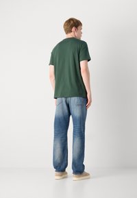 Grøn bomuld t-shirt med korte ærmer, parret med falmede blå denim jeans og lyse sko. Simpelt design uden synlige mønstre.
