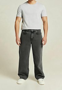 T-shirt gris, ajusté avec des manches courtes, associé à un jean gris foncé à jambes larges avec poches avant, fermeture à boutons et passants pour ceinture. Chaussures blanches.