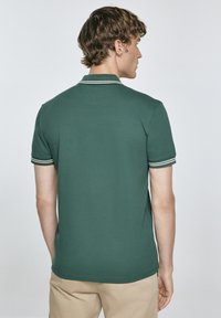Zelená polo košile s krátkými rukávy, se zásadními bílými a tmavě zelenými pruhy na manžetách, vyrobená z hladké texturované látky.