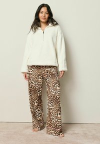 Fleece pullover i creme med halv lynlås og brede ærmer, parret med løse leopardprint bukser med en lyserød kant i nedre del.
