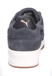 Sneaker in suede blu navy con logo Puma dorato sul tallone, suola intermedia bianca e suola esterna in gomma marrone, dotata di un colletto imbottito per il comfort.