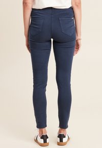 Navyblauwe skinny jeans met achterzakdetails, gemaakt van een soepele katoenmix, gecombineerd met wit en zwarte sneakers.