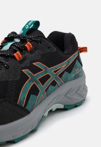 Chaussure de course noire avec des accents turquoise et orange. Présente un empeigne en mesh respirant, un motif en zigzag et une semelle en caoutchouc texturé. Détails réfléchissants inclus.