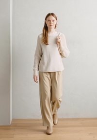 Maglione a coste color beige chiaro con collo alto, abbinato a pantaloni beige larghi e stivali alla caviglia abbinati. Tessuto liscio e design minimale.
