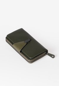 Groene leren portemonnee met een gestructureerde afwerking, ritssluiting en contrasterende gladde accenten. Voorzien van een drukknop en afgeronde hoeken.