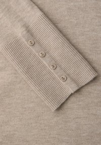 Pull en tricot beige avec des poignets côtelés ornés de quatre petits boutons. Texture douce avec une finition lisse et uniforme sur tout le tissu.