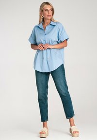 Jasnoniebieska koszula z krótkim rękawem zapinana na guziki, ozdobiona haftami, w połączeniu z dżinsami o wysokim stanie i sandałami na platformach.