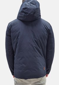 Giacca con cappuccio di colore blu navy con una texture liscia e gonfia; caratterizzata da un cappuccio regolabile e un accento arancione vicino all'orlo. Vista posteriore mostrata.