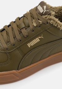 Zapatilla Puma verde oliva con cordones marrones, forro de felpa y suela de goma, con el logo de Puma en el lateral y la lengüeta.