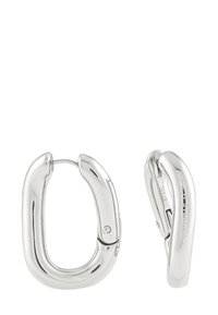 Une paire de boucles d'oreilles ovales en argent brillant avec des fermoirs à charnière sécurisés, dont l'une présente un logo gravé sur le côté.