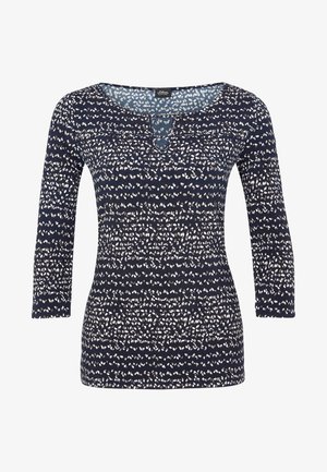 Camisa azul marino de manga larga con estampado de puntos blancos irregulares y pequeño escote con corte en forma de ojo de cerradura.