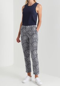 Navy sleeveless top paired with patterned trousers in white and navy featuring a geometric design. Footwear: white sneakers.