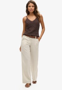 Top a maniche corte lavorato a maglia marrone con spalline sottili, abbinato a pantaloni larghi in lino beige chiaro e una cintura intrecciata marrone.
