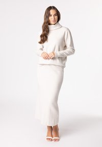 Cream pullover with a high collar and a fitted silhouette, paired with a matching long, textured skirt; both feature a grid pattern.